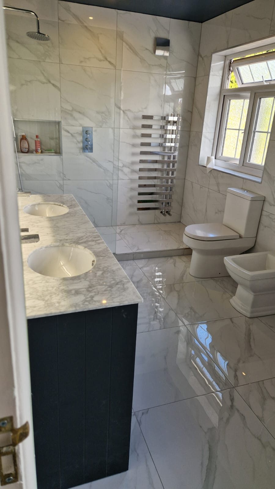 Marble family bathroom with twin basins and chrome towel rail