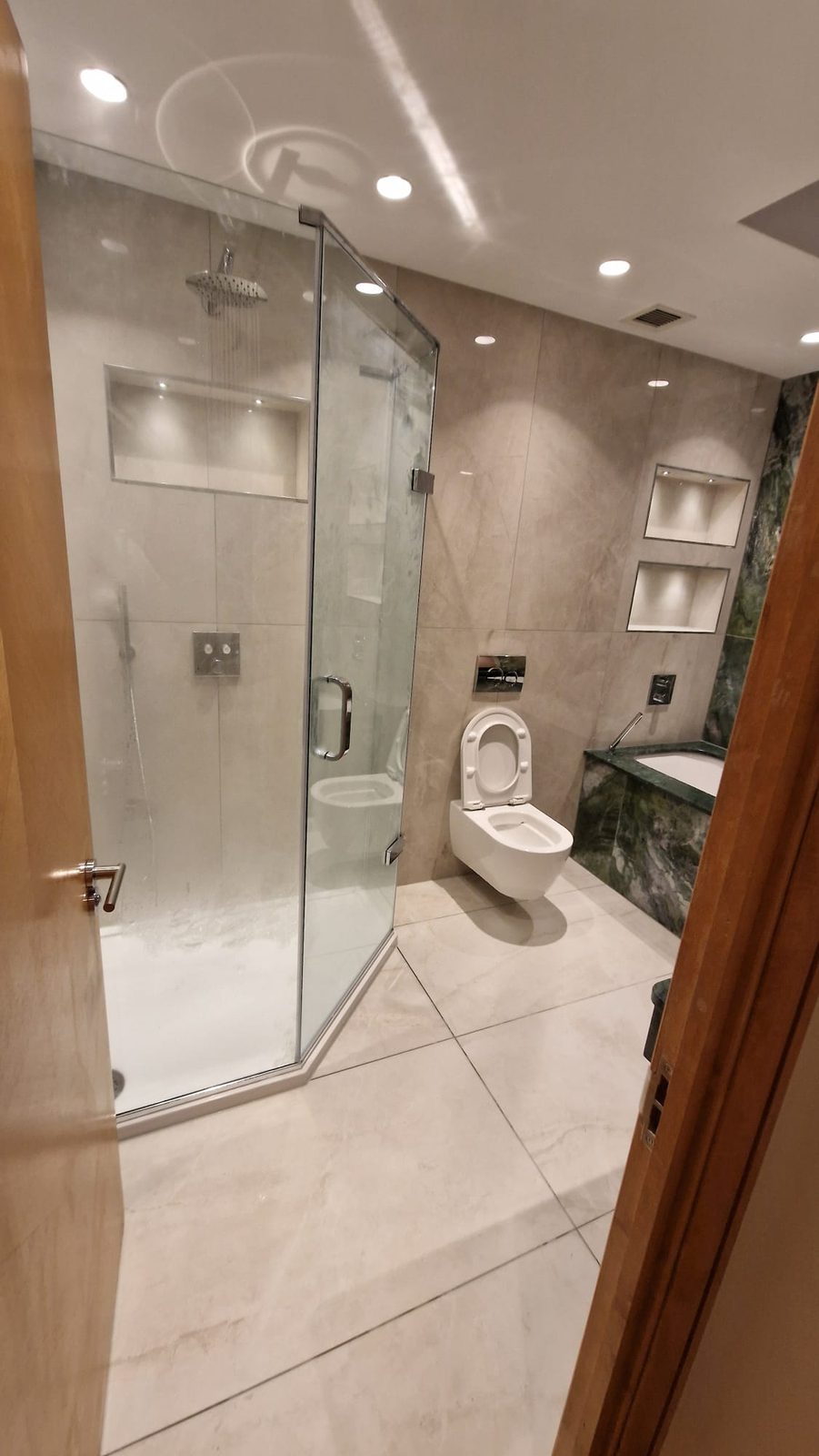 Walk-in rainfall shower with glass screen and lit niches